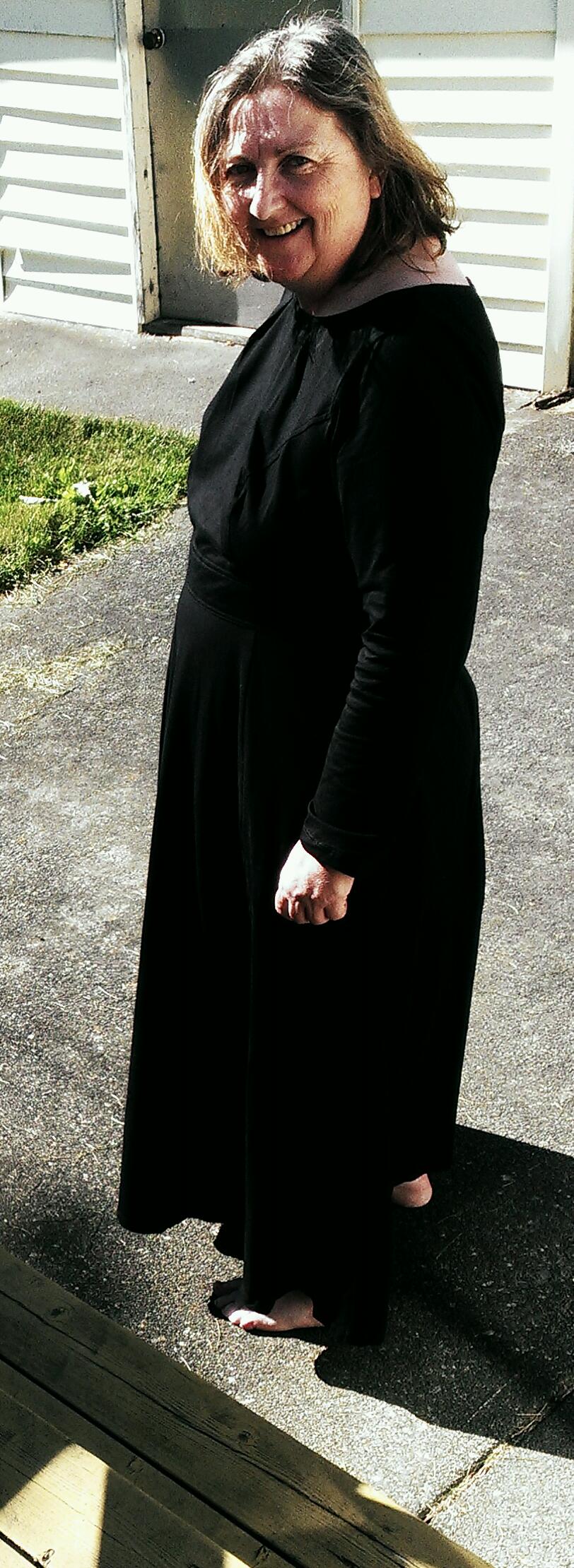 a middle aged white woman with medium length hair wears a long, long-sleeved black dress and bare feet
